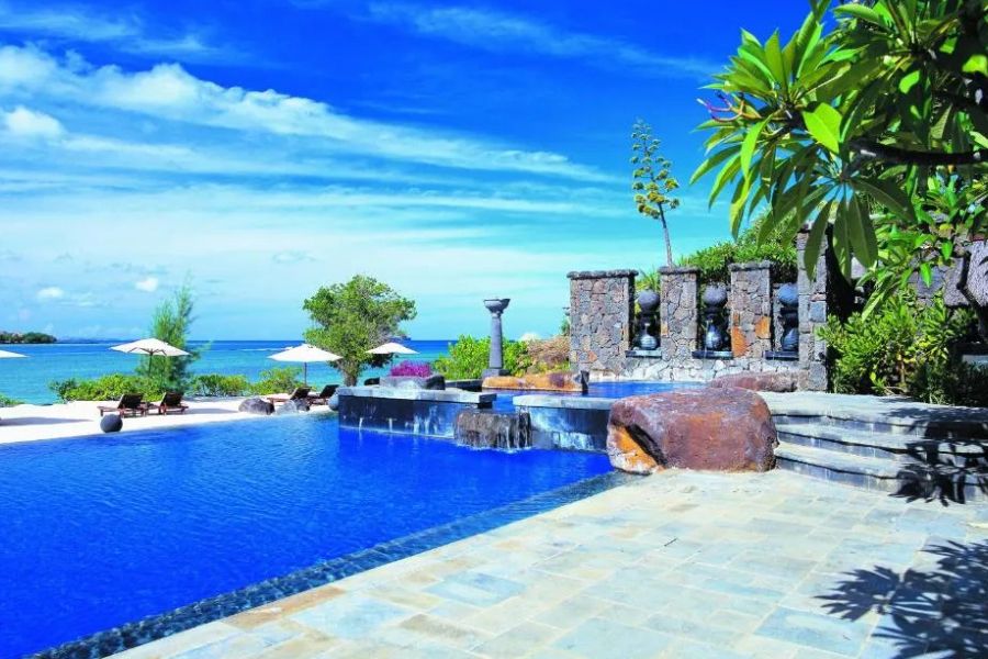 Resort swimming pool with stone fountains and ocean view under a blue sky