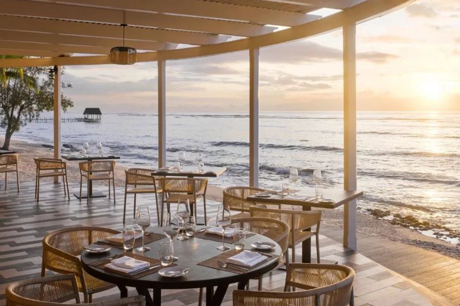 Open-air beachfront restaurant dining area overlooking the ocean at sunset