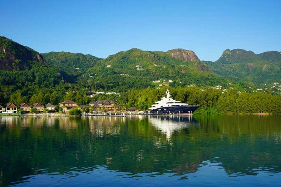 Large luxury yacht docked in a calm bay surrounded by green tropical mountains