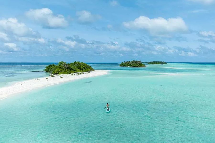 Person stand-up paddleboarding in turquoise water near tropical islands