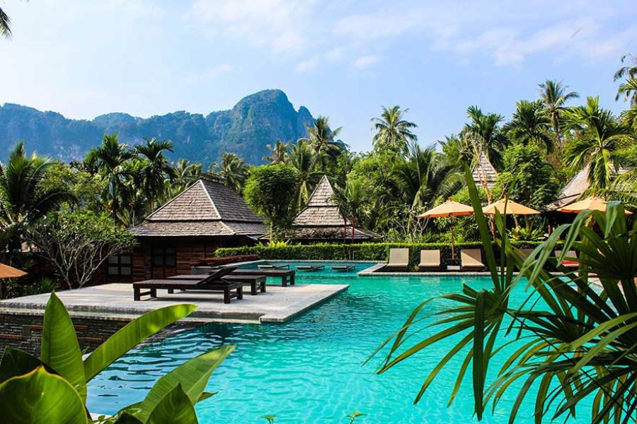 Tropical resort pool with sun loungers, palm trees, and mountain views