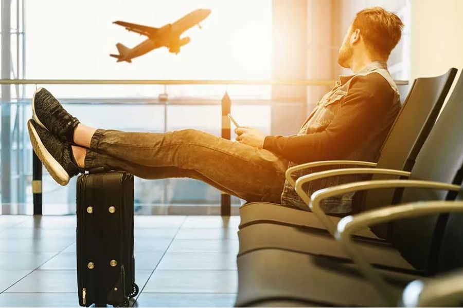 Man relaxing at airport terminal with feet on suitcase as plane takes off