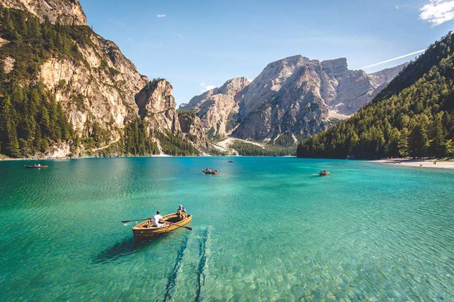 People rowing wooden boats on a clear alpine lake surrounded by mountains