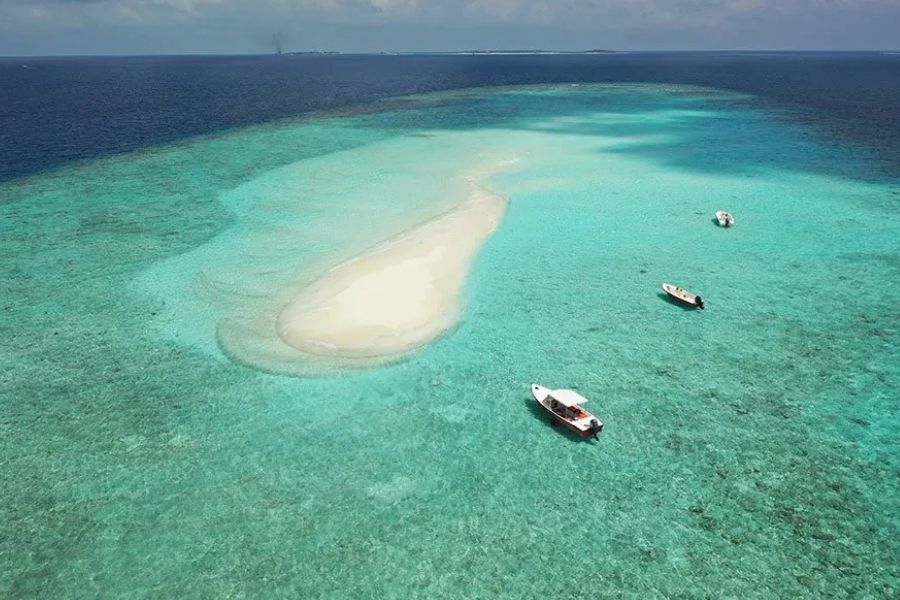 Aerial view of a small sandbank in the Maldives surrounded by turquoise reef, with boats nearby