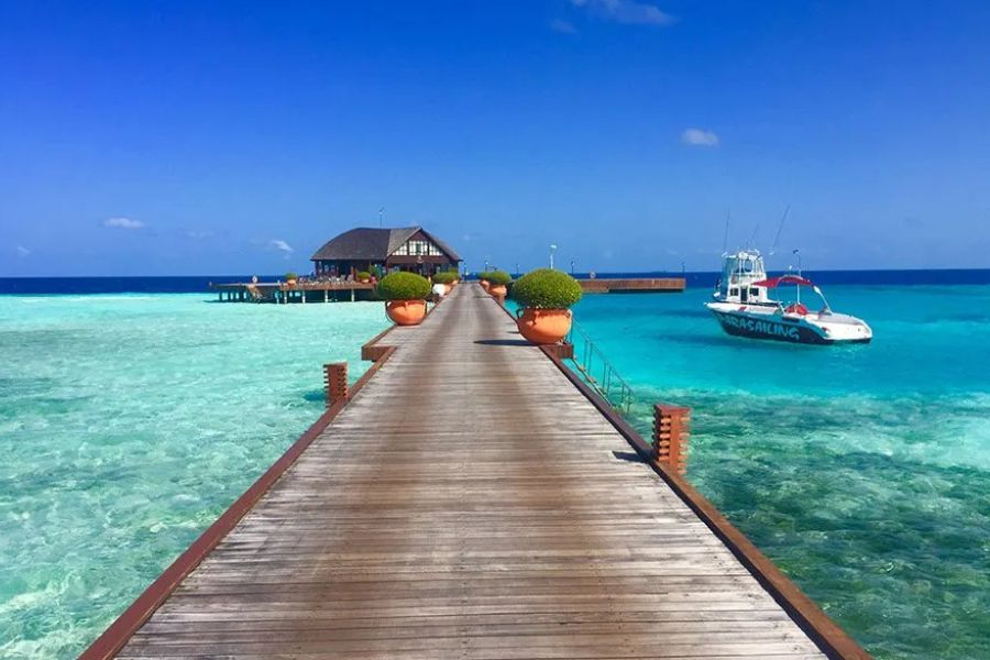 Wooden jetty to an overwater lounge in the Maldives, with a boat moored in the turquoise lagoon