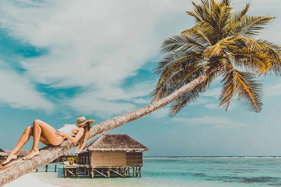 Woman relaxing on a leaning palm tree above overwater bungalows and lagoon in the Maldives