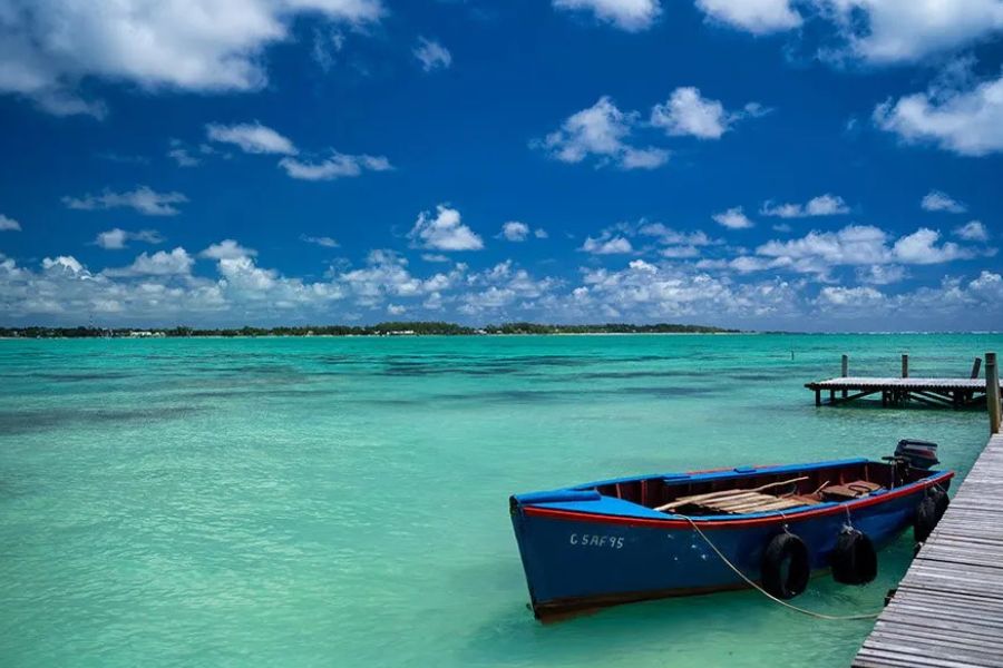 Small blue fishing boat tied to a wooden jetty in shallow turquoise lagoon water on the Mauritius coast
