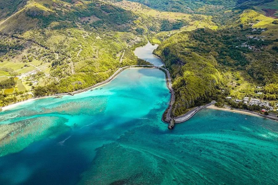Aerial view of a river mouth meeting the turquoise ocean, framed by lush green hills on the coast