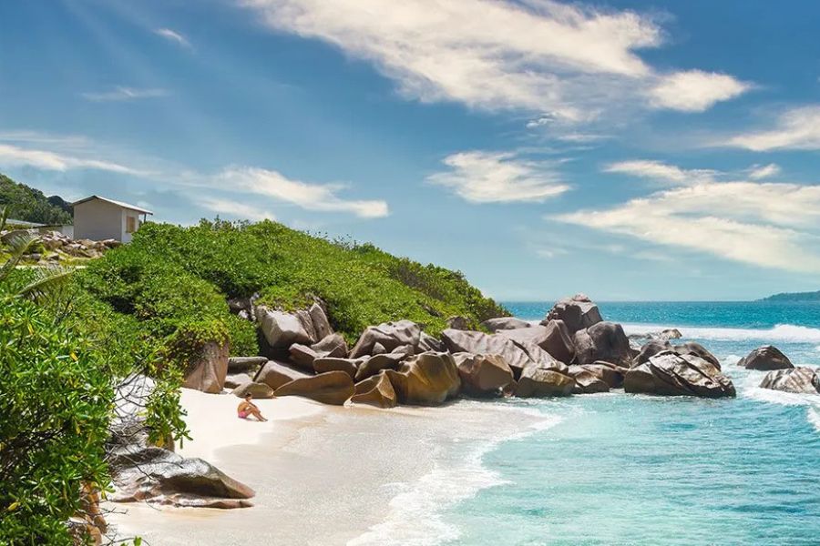 Granite boulders and turquoise water on a Seychelles island beach, with a visitor relaxing in the sea