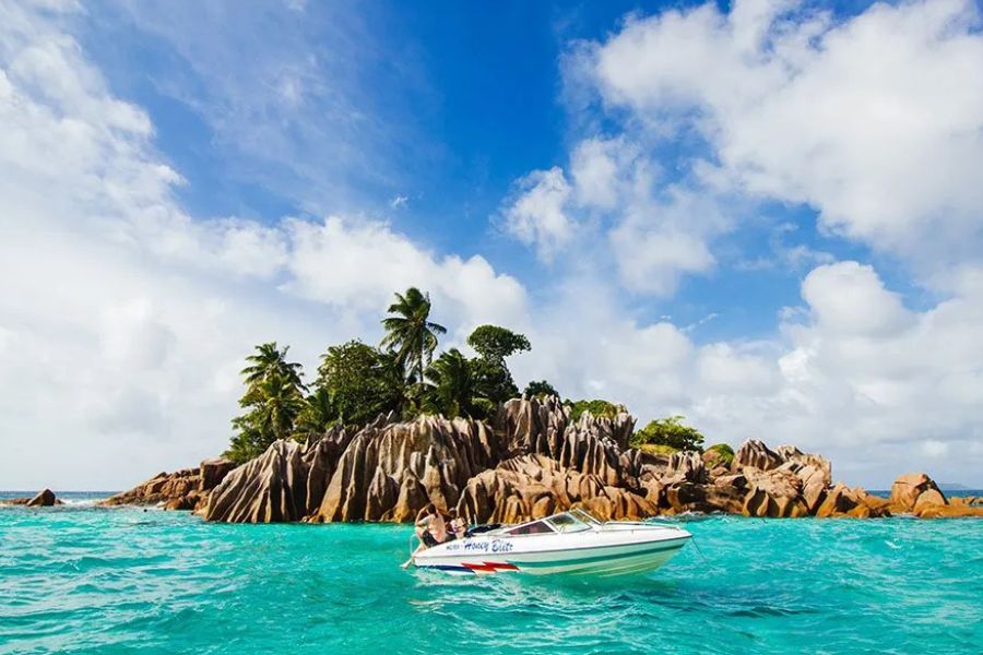 Small speedboat cruising past a granite islet with palm trees during island-hopping in the Seychelles