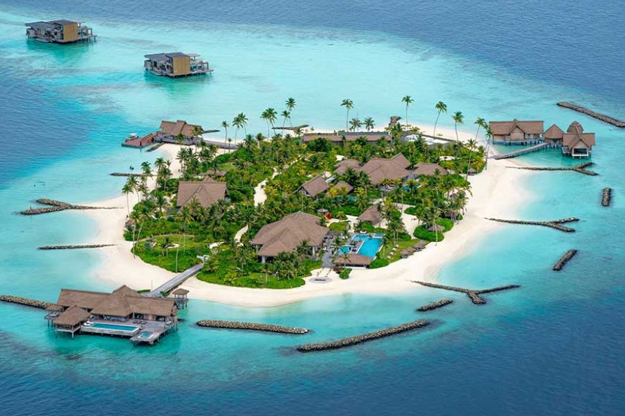 Aerial view of an overwater bungalow resort island in the Maldives, surrounded by turquoise lagoon