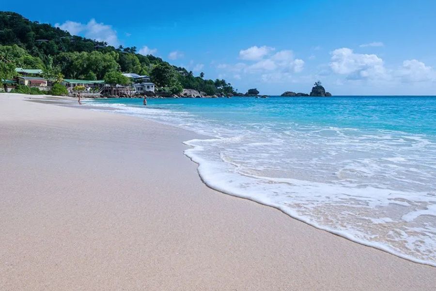 Pristine white sand beach with gentle waves and lush green hills along turquoise sea