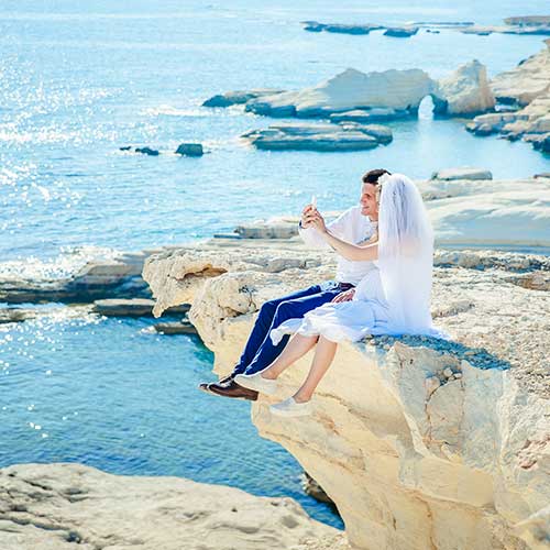 Bride and groom taking a photo together on a rocky coastal cliff above the sea