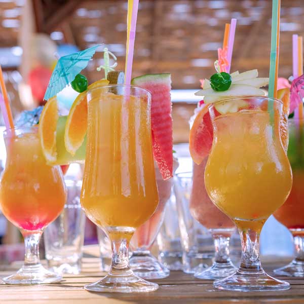 Row of colourful tropical cocktails garnished with fruit at a beach bar