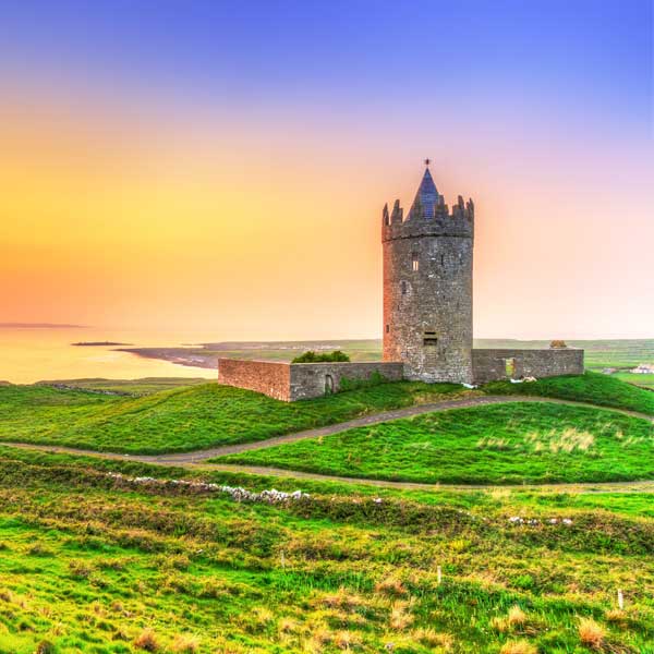 Stone round tower on an Irish coastal hillside at sunset