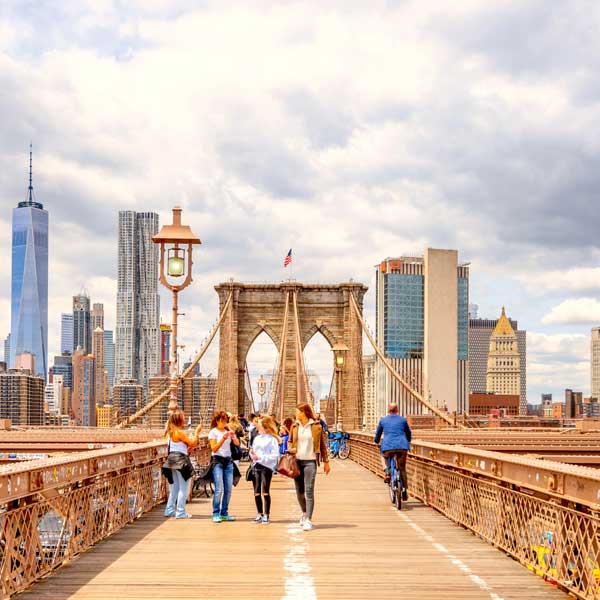 Travellers walking across the Brooklyn Bridge with the New York City skyline behind them
