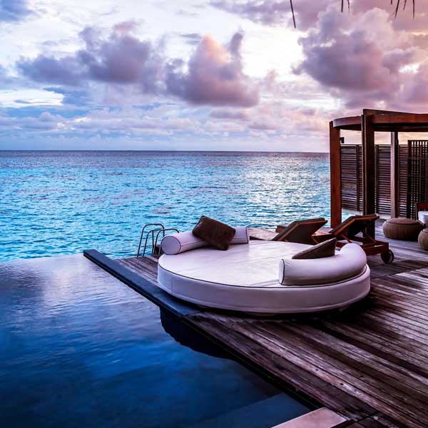 Round daybed on an overwater villa deck overlooking the ocean at sunset