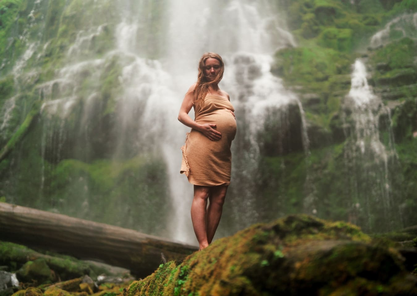 Expecting mother standing near a waterfall during a maternity session in Central Oregon