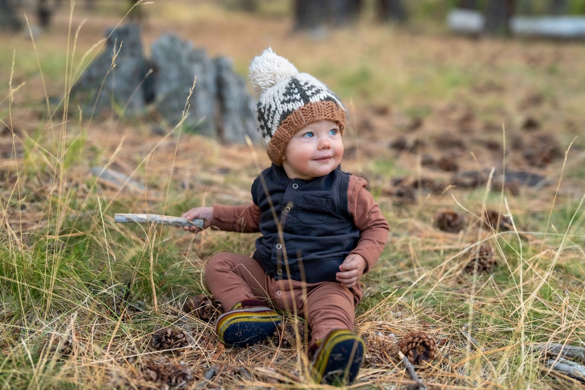 Baby in knit hat sitting in a forest meadow