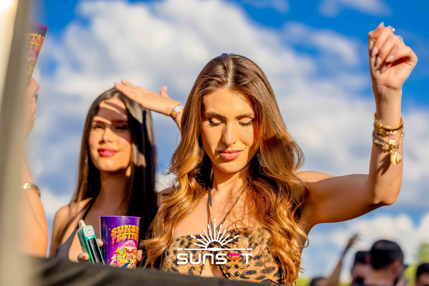 Duas amigas dançam sob o céu azul e a luz da tarde no Sunset Festival 2025.