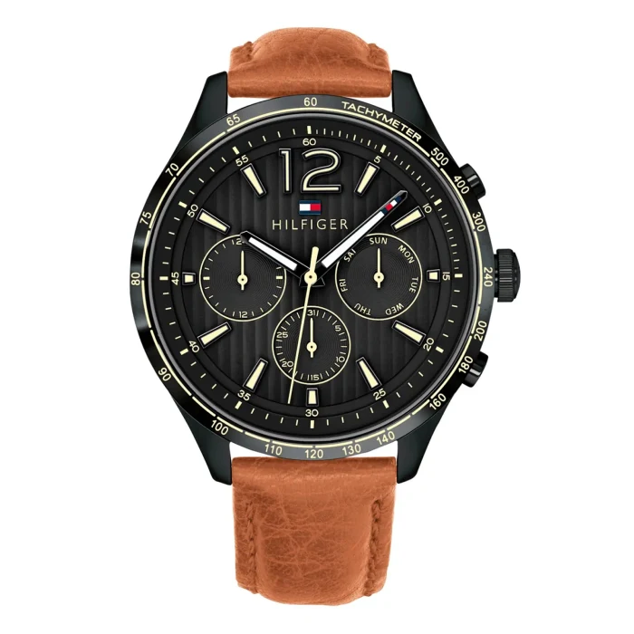 Black and gold Tom Hilfiger watch with a tachymeter, featuring three sub-dials and a brown leather strap. Stylish and modern design.