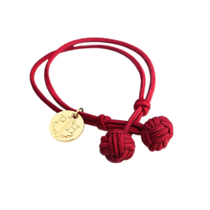 PAUL HEWITT PH-KB-R-L-S A red bracelet featuring three decorative knots and a gold pendant with initials and an anchor design.