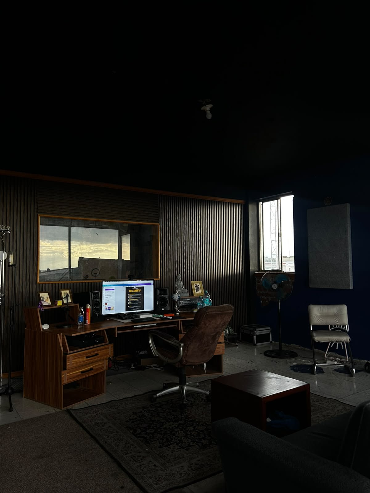 Sala de control de Sacred Room Studio: escritorio con monitores, paneles de madera y ventana a la cabina