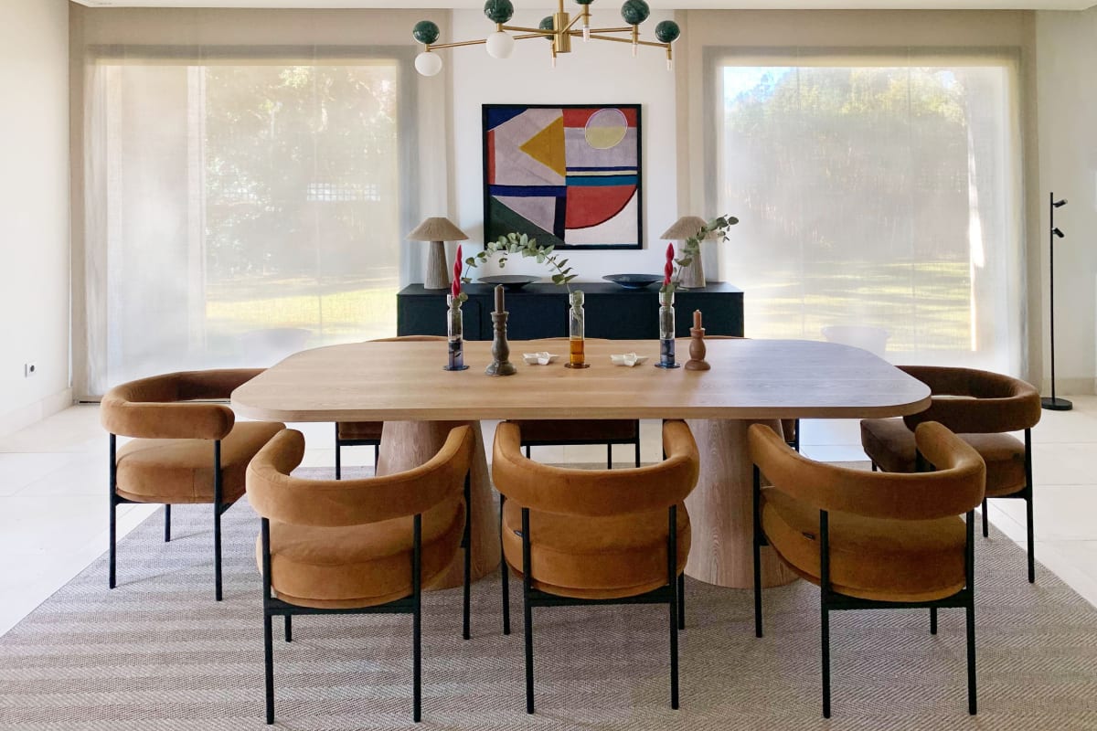 Dining room with a wooden table, upholstered chairs, and a sideboard with abstract art on the wall.
