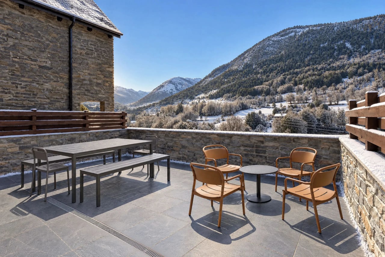 Large terrace with slate floor and high stone walls, outdoor dining table with benches and chairs, armchairs and snowy mountain views.