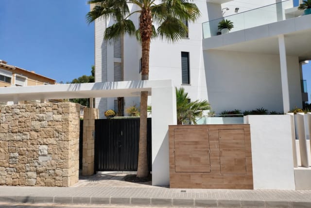 Entrance to the house with a black gate, stone wall, and white facade.
