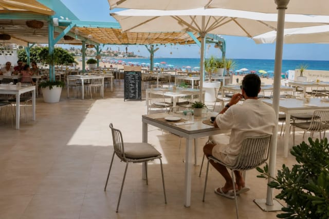 Outdoor restaurant with tables and chairs, with the beach and sea in the background.