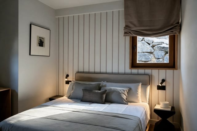 Bedroom with a double bed, nightstands, and a window with a view of a stone wall.