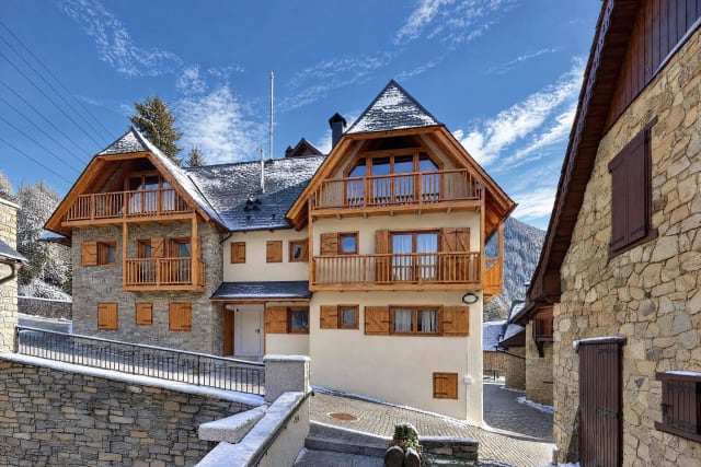 Exterior of the building in the village, with a light dusting of snow on the slate roofs, wooden balconies and the neighbouring stone houses.