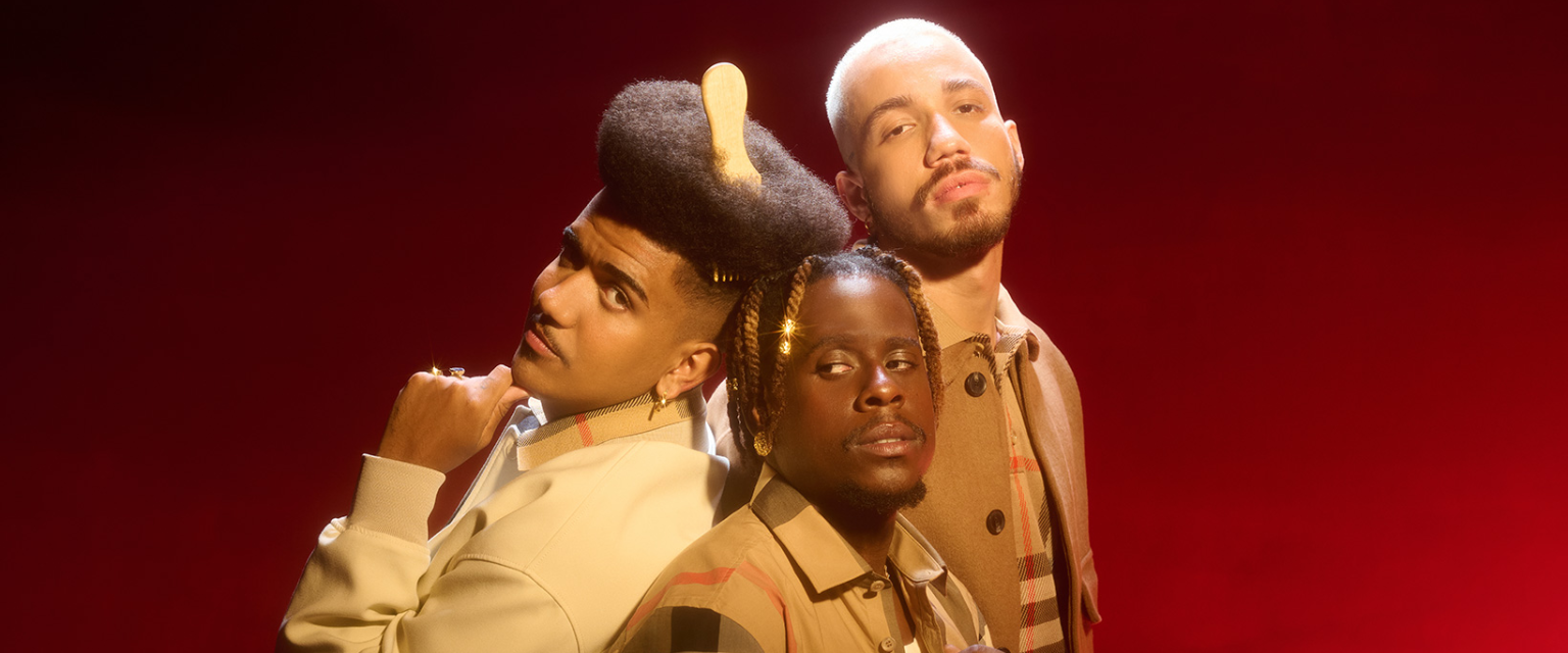 Trio de homens negros posando de costas uns para os outros enquanto olham para a câmera. Foto de Pedro Miceli.