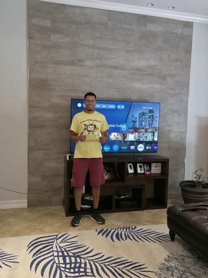 Tarick, owner of Tarick's TV Mounting, next to a TV mounted on a gray tile accent wall in a Melbourne, FL living room