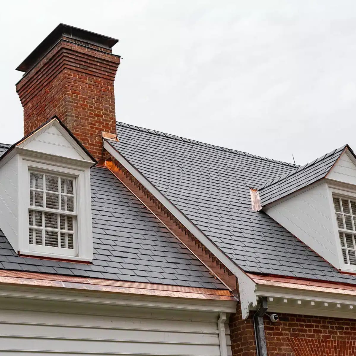 Gray slate roof with copper valleys and copper-trimmed dormers beside a brick chimney