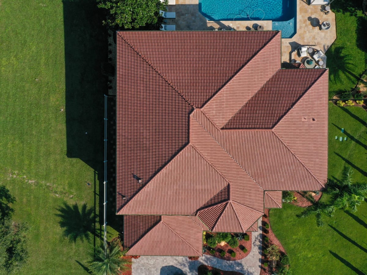Overhead drone view of a red clay tile roof above a pool and patio