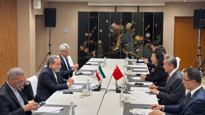 A bilateral diplomatic meeting between Iranian and Chinese delegations seated across a conference table, with Iranian and Chinese flags displayed in the center and a decorative Chinese folding screen in the background.
