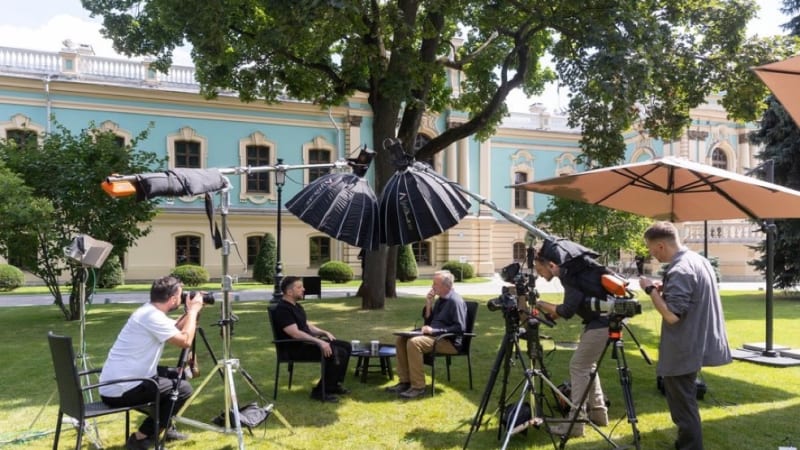 An outdoor television interview setup on the grounds of the Mariinskyi Palace in Kyiv, with two men seated for an interview surrounded by camera operators, lighting equipment, and professional video cameras on tripods.