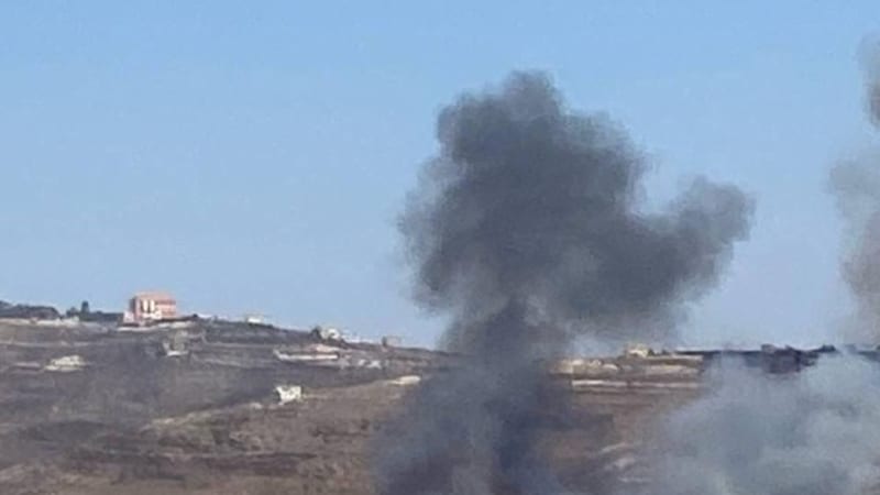 Smoke rising from an area in a hilly, arid landscape with scattered buildings, consistent with an airstrike or shelling in the Middle East region.