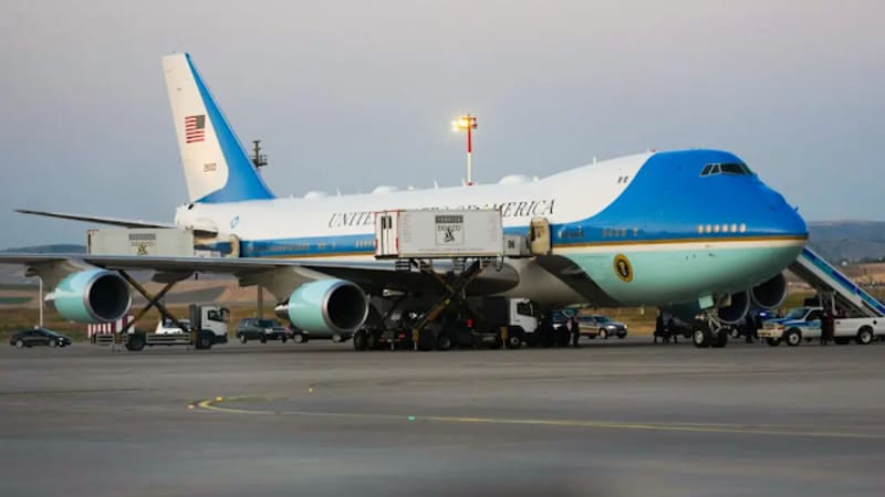 Air Force One, the United States presidential Boeing 747 (VC-25A), parked on a tarmac with ground support vehicles and personnel nearby during dusk or dawn lighting.