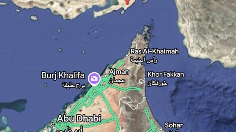 Google Maps satellite view of the Strait of Hormuz region showing a red pin marker in the strait between Bandar Abbas, Iran and the UAE coast, with visible labels for Abu Dhabi, Ajman, Ras Al-Khaimah, and Burj Khalifa.