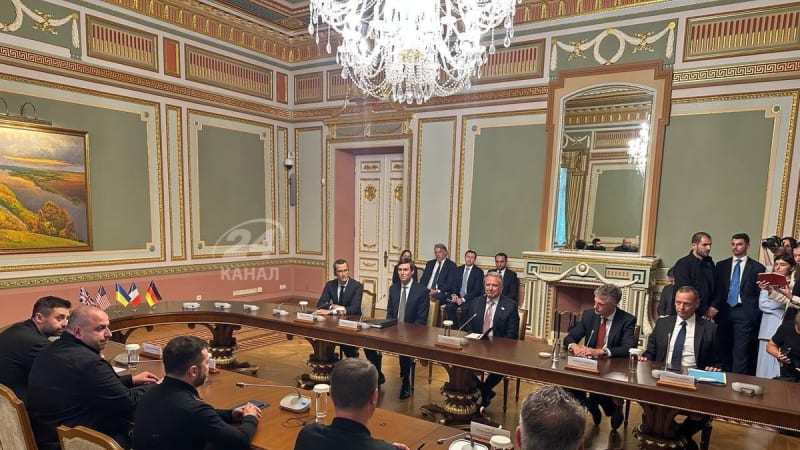 A high-level diplomatic meeting in an ornate government hall in Kyiv, with officials seated around a large curved conference table. Multiple national flags including those of the UK, US, Ukraine, France, and Germany are visible in the background. The image bears a 24 Kanal watermark.