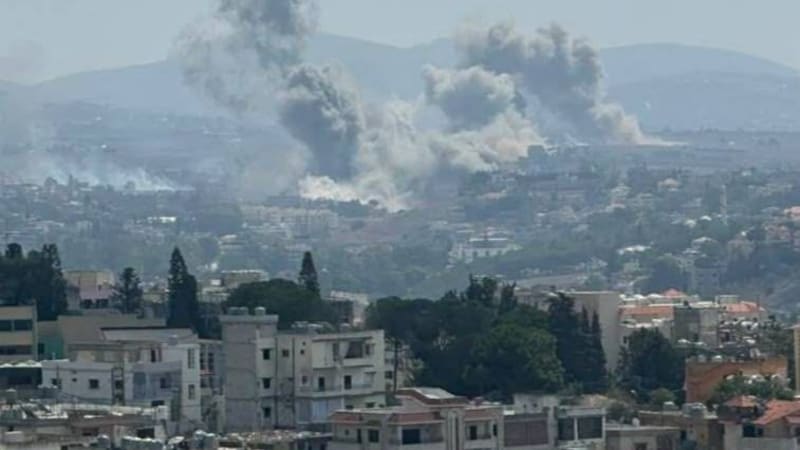 Multiple plumes of smoke rising from airstrikes or explosions over a densely built urban area with hills in the background, consistent with conflict zone imagery from the Middle East.