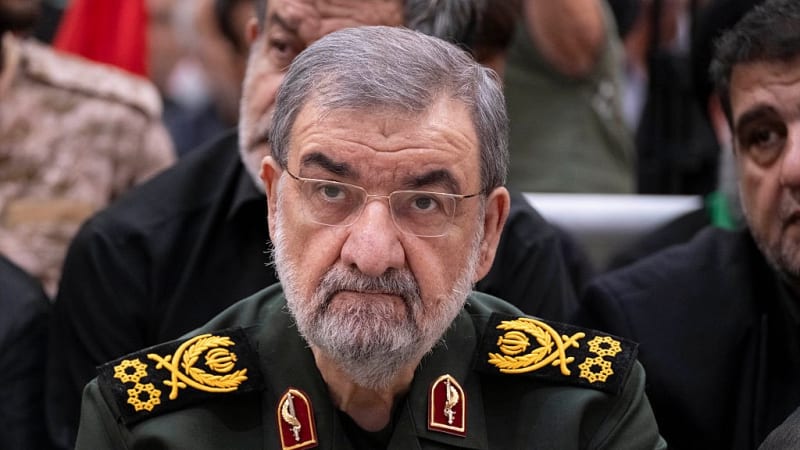 A senior Iranian military official wearing an IRGC (Islamic Revolutionary Guard Corps) uniform with major general rank insignia, seated at a formal event among other attendees.