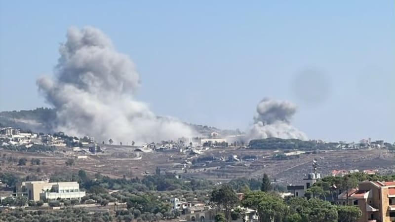 Multiple plumes of smoke rising from airstrikes or explosions on hillside towns, viewed from a distance across a Mediterranean-style landscape with residential buildings and vegetation in the foreground, likely southern Lebanon.