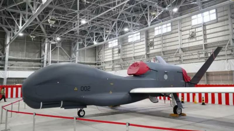 A large grey RQ-4 Global Hawk unmanned aerial vehicle (UAV) numbered 002 displayed inside a military hangar, likely belonging to the Japan Air Self-Defense Force.