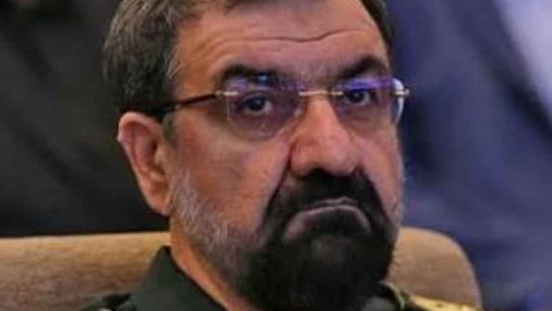 A man in an Iranian military uniform with general's insignia, wearing glasses and a goatee, seated at what appears to be an official event or conference.