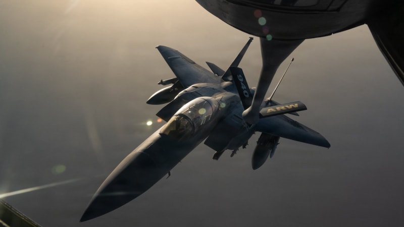A U.S. Air Force F-15E Strike Eagle approaches a refueling boom from a 940th Air Refueling Wing (ARW) tanker aircraft during an aerial refueling operation, photographed at dusk or dawn with dramatic lighting.