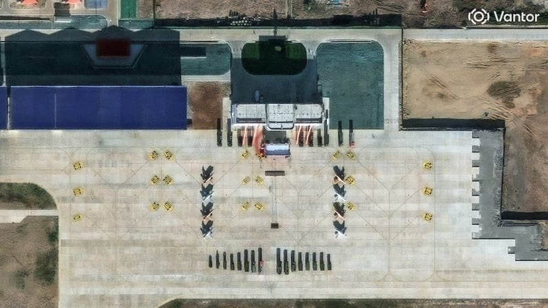 Satellite imagery showing a military airfield apron with multiple fighter aircraft parked in formation, ground support vehicles, and hangars, watermarked by Vantor.